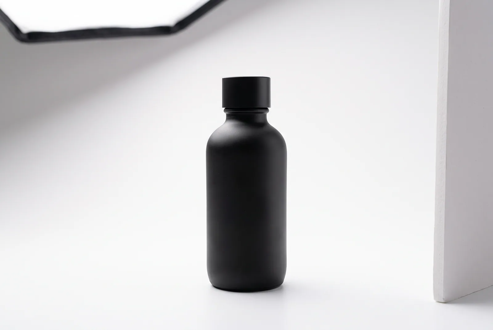 Mattschwarze Flasche auf weißem Hintergrund, seitlich beleuchtet von einer Softbox, rechts ein weißer Reflektor